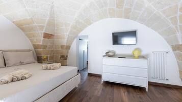 Un dormitorio con techo de piedra, una cama con toallas enrolladas, un tocador blanco y un televisor de pantalla plana.