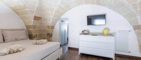 Un dormitorio con techo de piedra, una cama con toallas enrolladas, un tocador blanco y un televisor de pantalla plana.