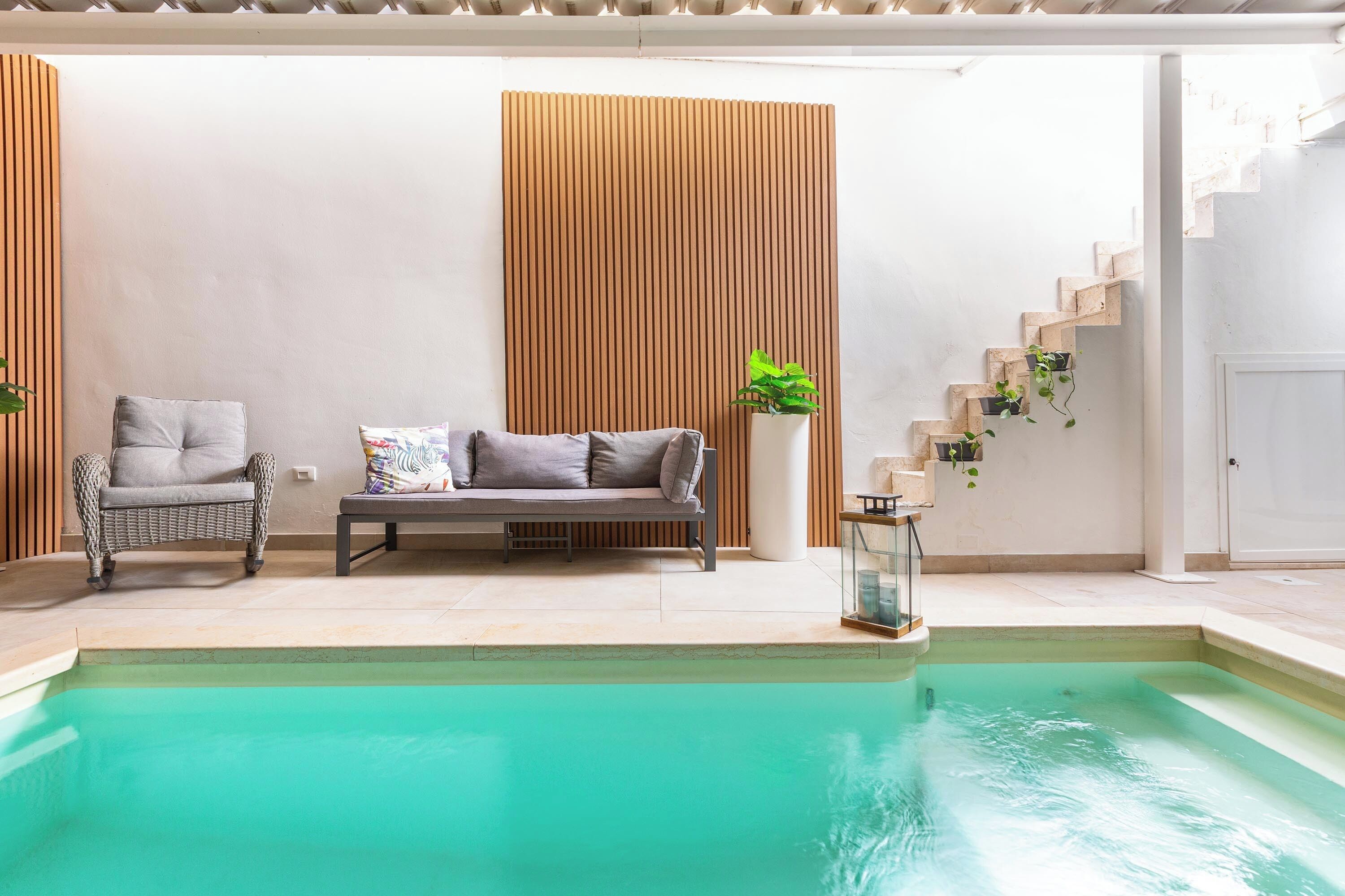 A pool area with a sofa and chairs, a wooden panel wall, and a staircase.