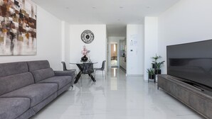 A modern living room with a grey sofa, a dining table with chairs, a TV on a wooden stand, and a large abstract painting on the wall. - 4153 Pasitea Luxury Suite by Barbarhouse (Squinzano)