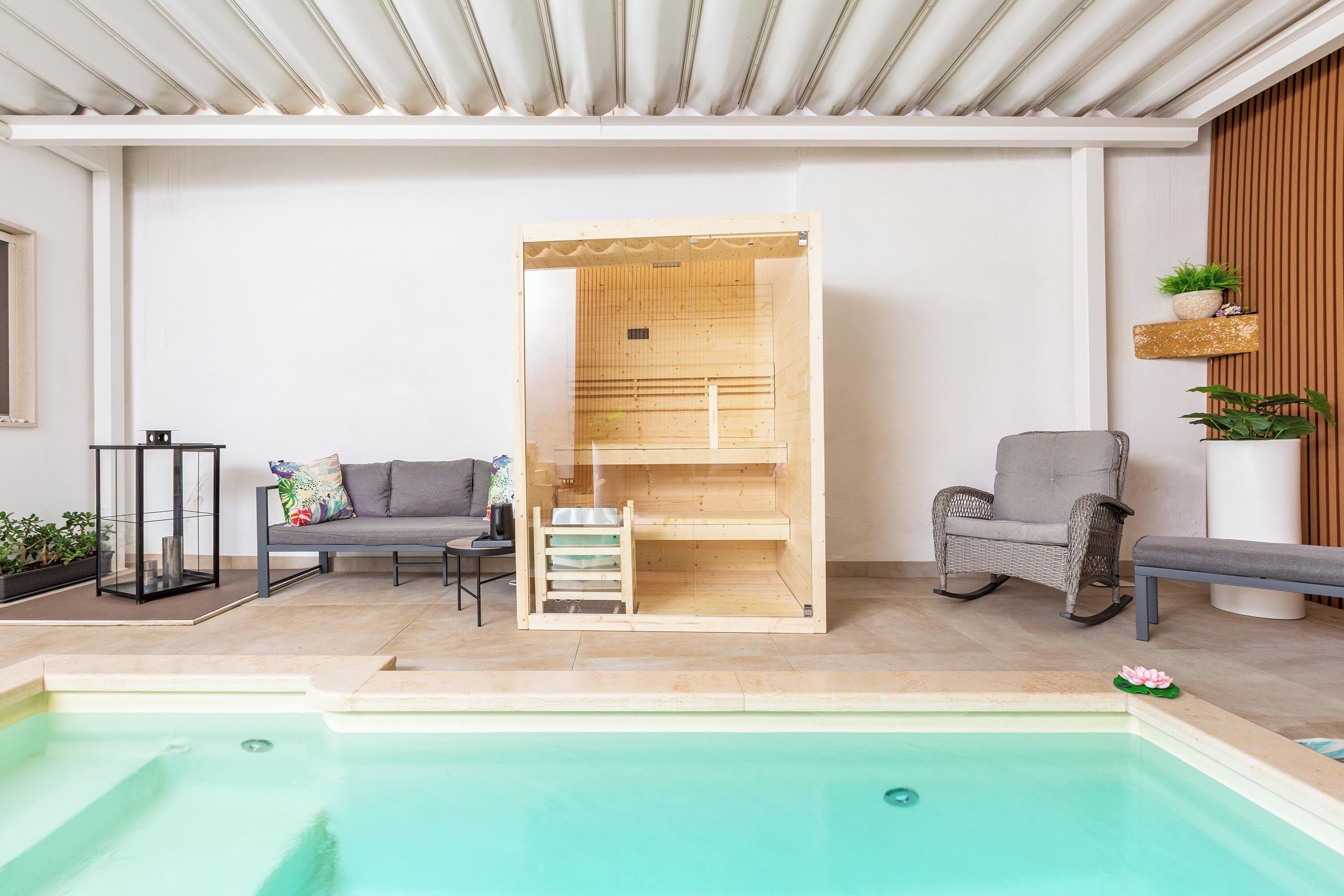 Un área de piscina interior moderna con sauna de madera, asientos y plantas en macetas.