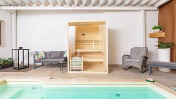 Un área de piscina interior moderna con sauna de madera, asientos y plantas en macetas.