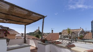 Eine Dachterrasse mit einer Pergola, einer Sitzgelegenheit und Blick auf einen Hügel mit einer Kirche.