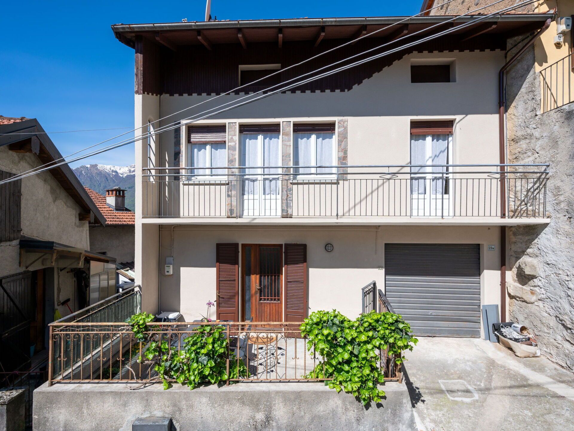 A two-story building with a balcony, a garage door, and a small garden area.