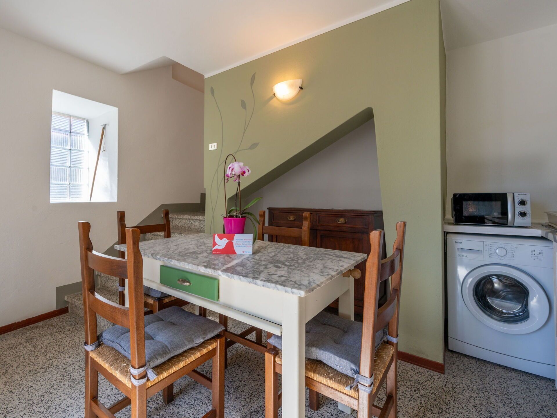 A dining area with a table, chairs, a potted orchid, and a microwave in the background.