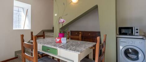 A dining area with a table, chairs, a potted orchid, and a microwave in the background.