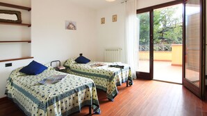 A bedroom with two beds, a radiator, a ceiling light, and a balcony with a view of trees. - Cosy apartment for 4 people with A/C, WIFI, TV and terrace (Pietrasanta)