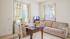A dining area with a wooden table, chairs, and a sofa. There are windows with curtains, a television, and a plant on the table. - Nice apartment for 3 guests with WIFI, TV and terrace (Camaiore)