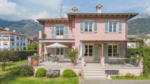 A pink two-story house with a balcony, a patio with outdoor furniture, and a mountain backdrop. - Nice apartment for 3 guests with WIFI, TV and terrace (Camaiore)