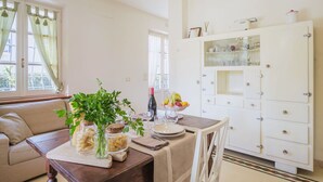 A dining area with a wooden table set for two, a white cabinet with glass doors, and a window with curtains. - Nice apartment for 3 guests with WIFI, TV and terrace (Camaiore)