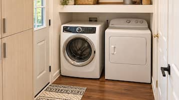 A laundry room with a washing machine, dryer, and shelves with baskets and plants.