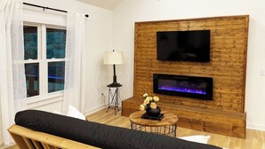 Een woonkamer met een houten wand, een flatscreen televisie, een open haard, een bank en een tafel met een bloemenvaas.