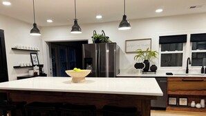 Een moderne keuken met een groot kookeiland, hangende lampen en een koelkast.