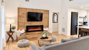 A modern living room with a fireplace, a flat-screen TV, and a dining area.