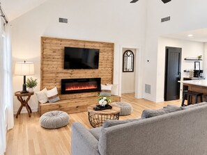 A modern living room with a fireplace, a flat-screen TV, and a dining area.