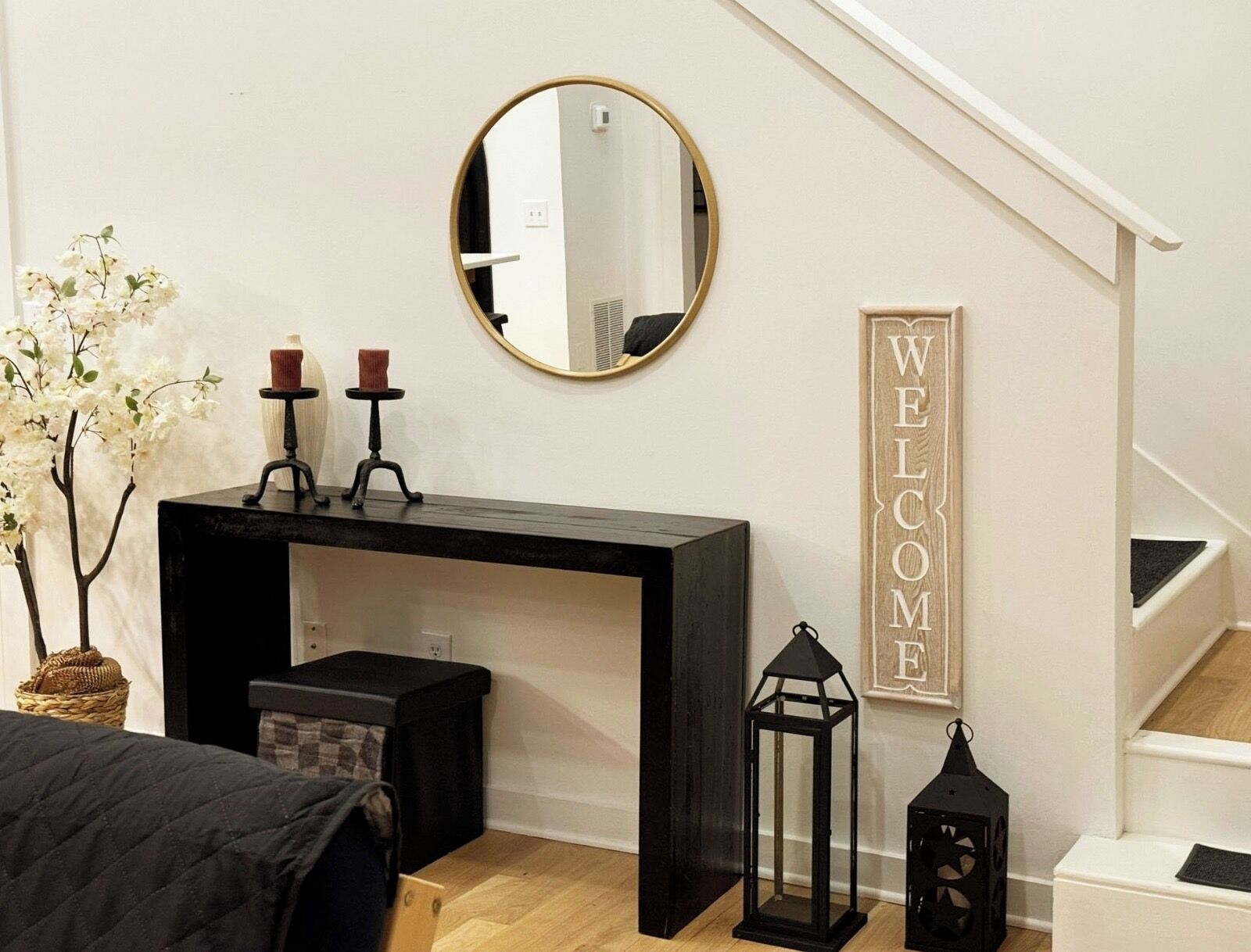 A bedroom with a bed, a desk, a mirror, a welcome sign, and a staircase.