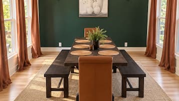 A dining room with a high ceiling, a dark green wall, a chandelier, a framed artwork, and a table set for four.