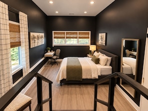 A bedroom with a bed, desk, chair, window with blinds, and a mirror.