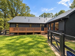 A two-story house with a deck, surrounded by a grassy yard and trees.