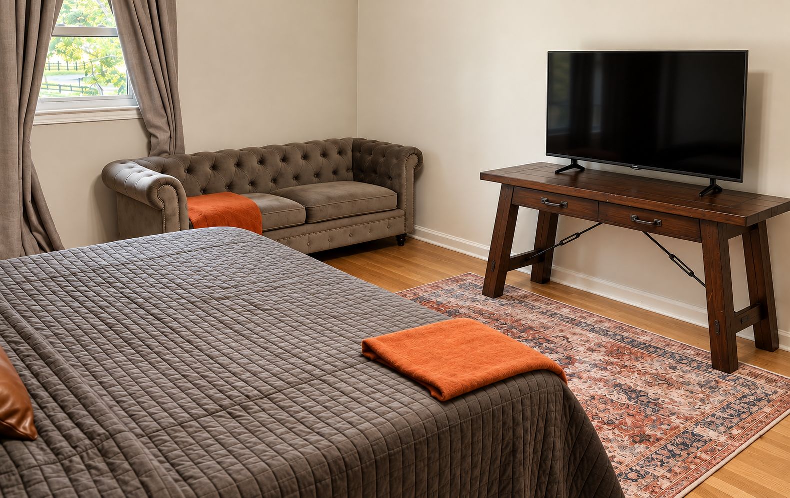 A bedroom with a large bed, a sofa, a television on a wooden table, and a patterned rug.