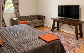 A bedroom with a large bed, a sofa, a television on a wooden table, and a patterned rug.