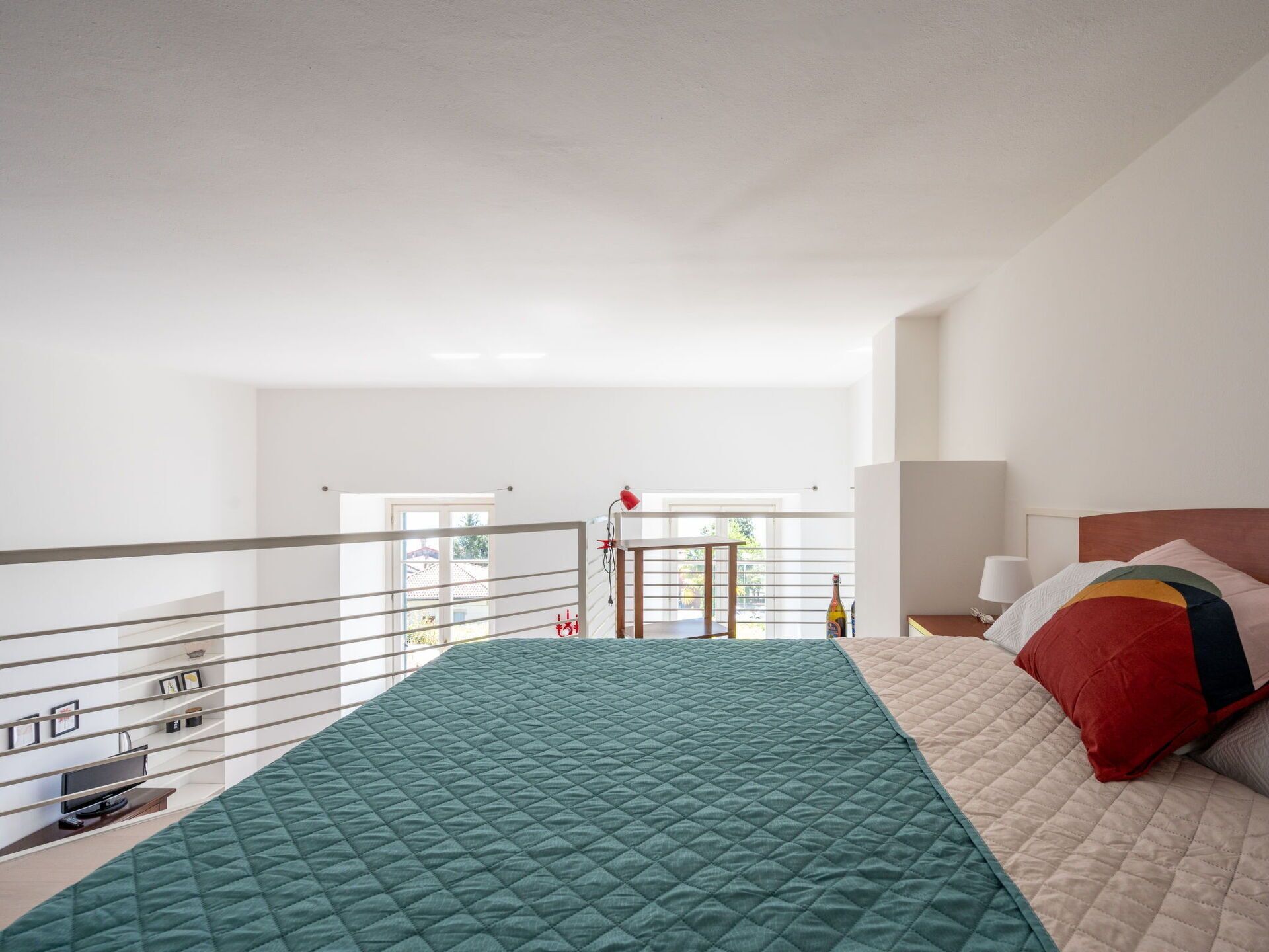 A bedroom with a green quilted bedspread, a wooden headboard, and a bedside table with a lamp.