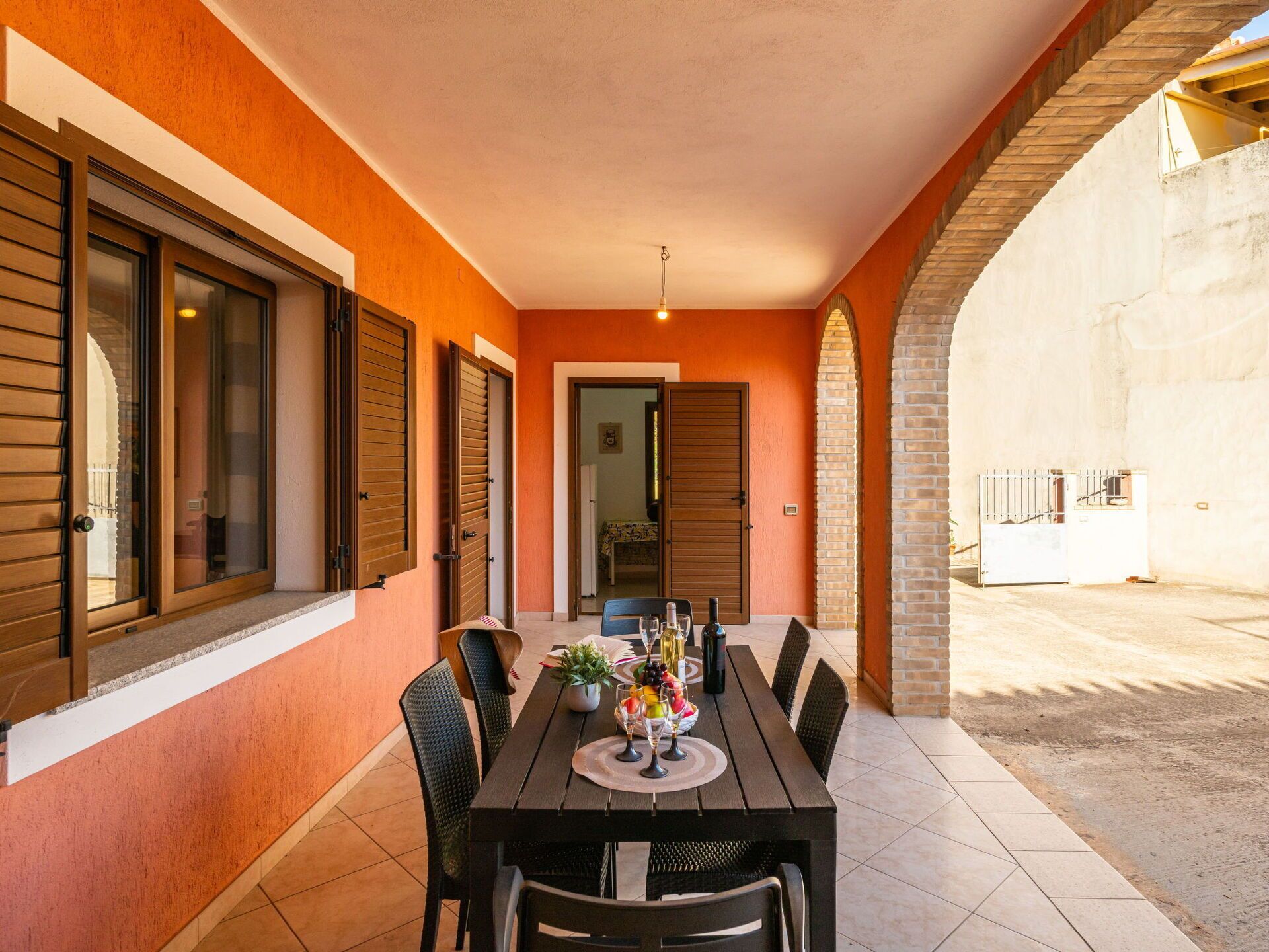 Un área de comedor al aire libre con una mesa preparada para cuatro personas, rodeada de sillas y vista a la calle.