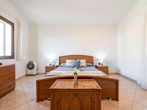 Ein Schlafzimmer mit einem hölzernen Bett, Nachttischen, einem kleinen Holzschrank und einem Ventilator.