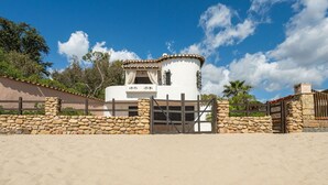 A white building with a stone wall and gate, surrounded by a sandy area and trees. - Cosy apartment in villa for 8 people with WIFI, A/C, TV and patio (Pula)