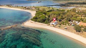 An aerial view of a coastal area with a beach, clear waters, and a house with a red flag. - Cosy apartment in villa for 8 people with WIFI, A/C, TV and patio (Pula)