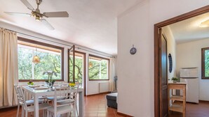 A dining area with a table set for four, large windows, a ceiling fan, and a view of greenery outside.