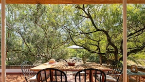 An outdoor dining area with a wooden table and chairs, surrounded by trees.