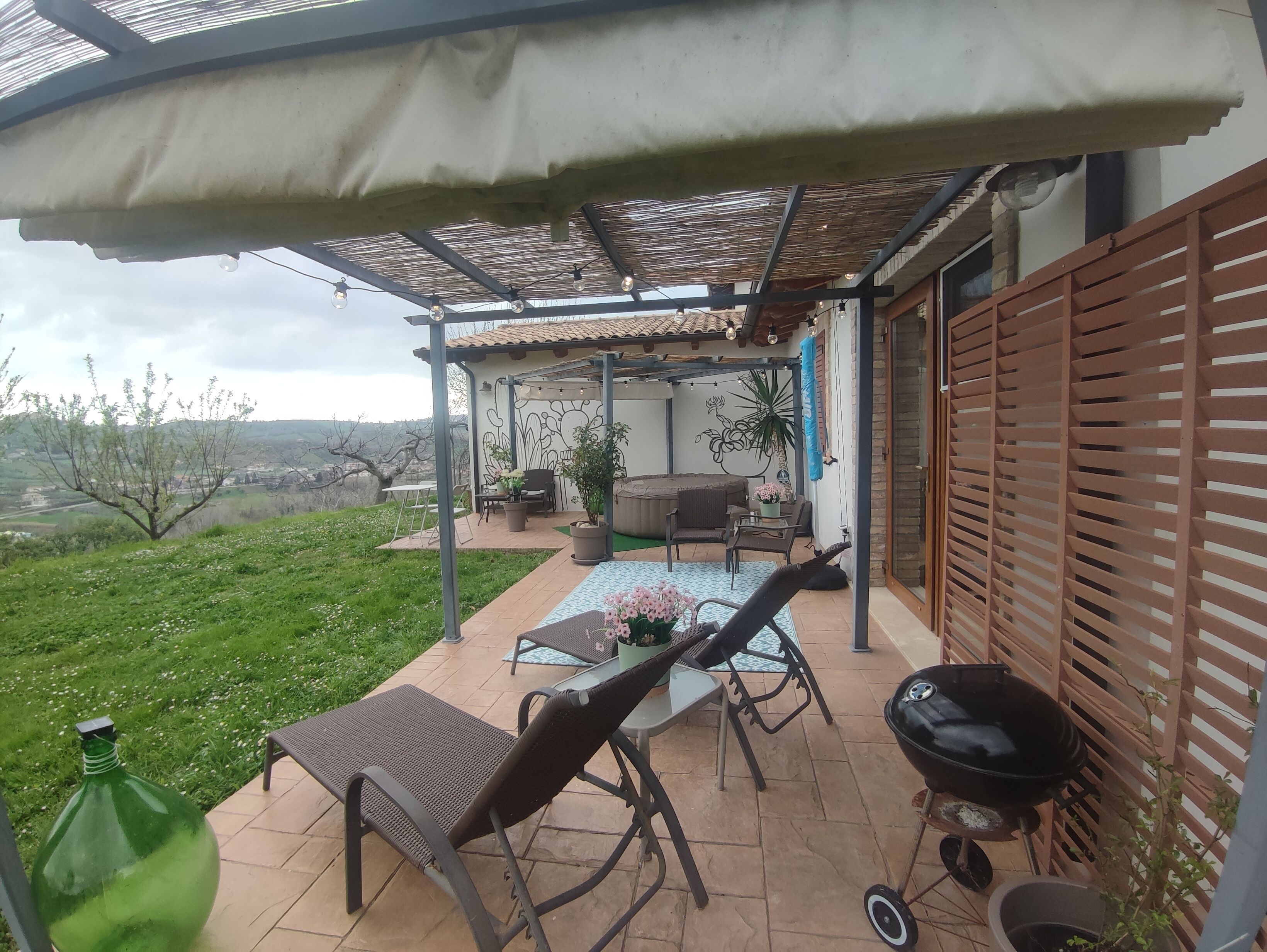 Eine überdachte Terrasse mit Gartenmöbeln, einem Grill und Blick ins Grüne.