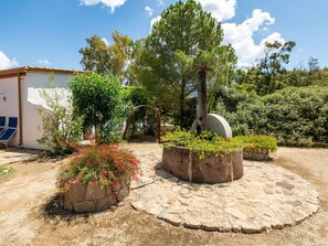A courtyard with stone planters, a pergola, and a white building with blue chairs.