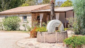 A stone building with a tiled roof, a stone well, and surrounding vegetation.