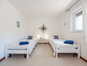 A room with two beds, a compass wall decoration, and a window with curtains.