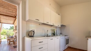 A compact kitchen with white cabinets, a built-in oven, and a dishwasher. There is a window with a view of greenery outside.