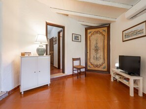 Sala de estar com um armário branco, uma luminária, uma poltrona, uma TV em um móvel e uma porta com detalhe decorativo.