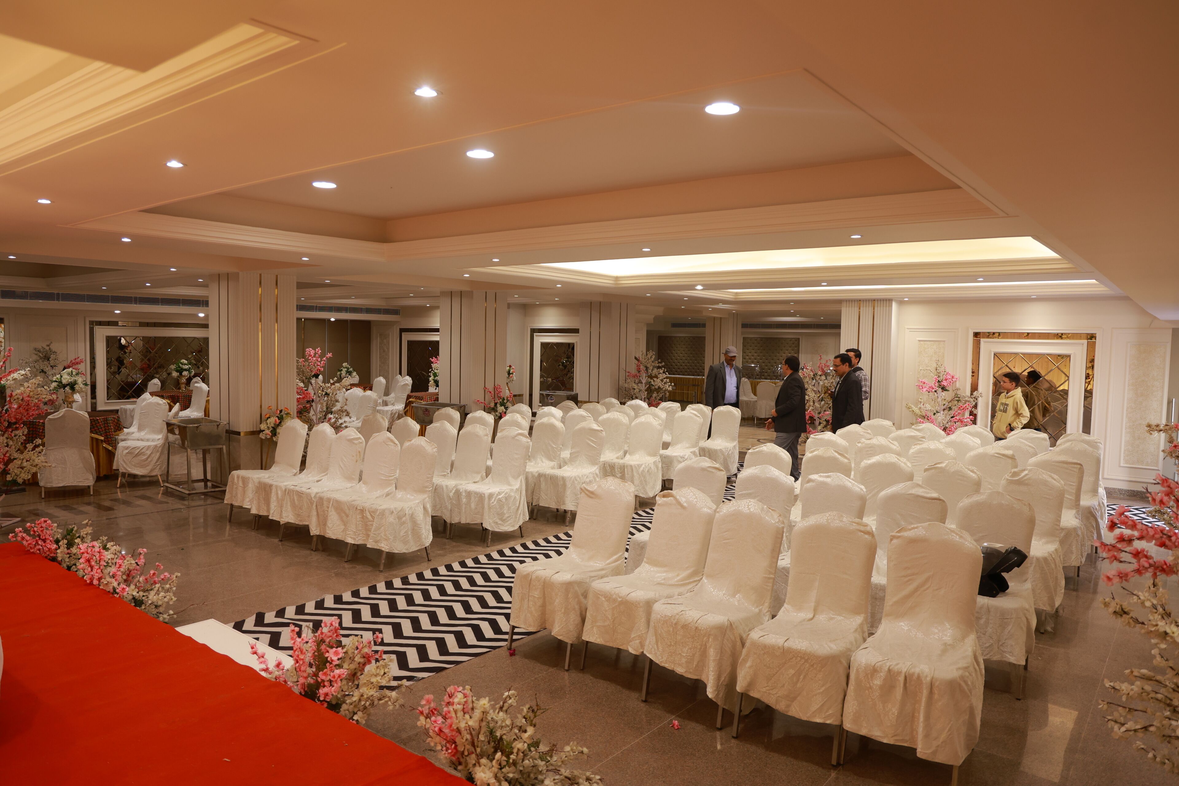 Un vaste hall orné de rangées de chaises blanches, d’un tapis rouge et de décorations florales.