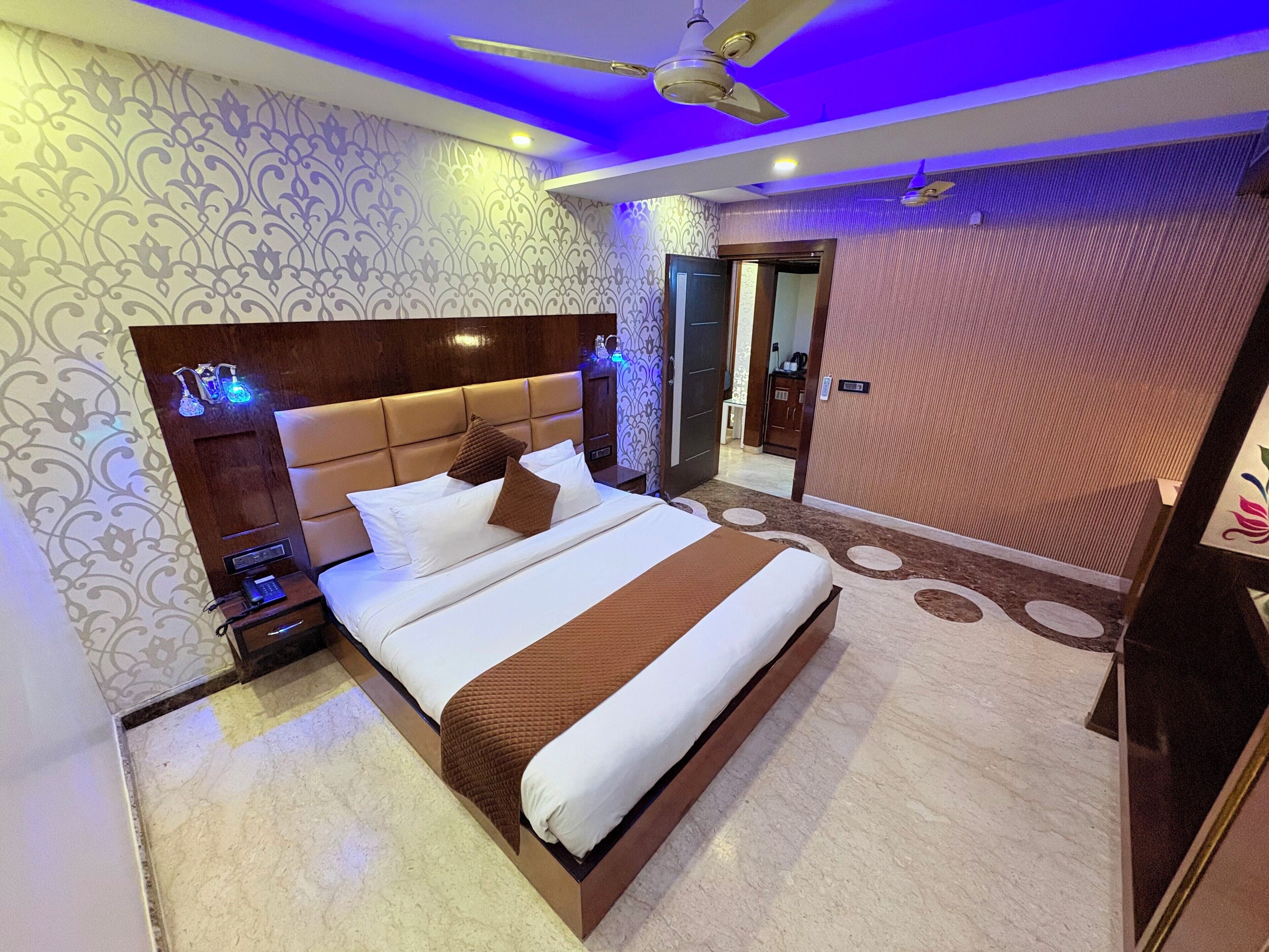 A modern bedroom with a large bed, a nightstand, a bedside table, a ceiling fan, and a bathroom visible through an open door.