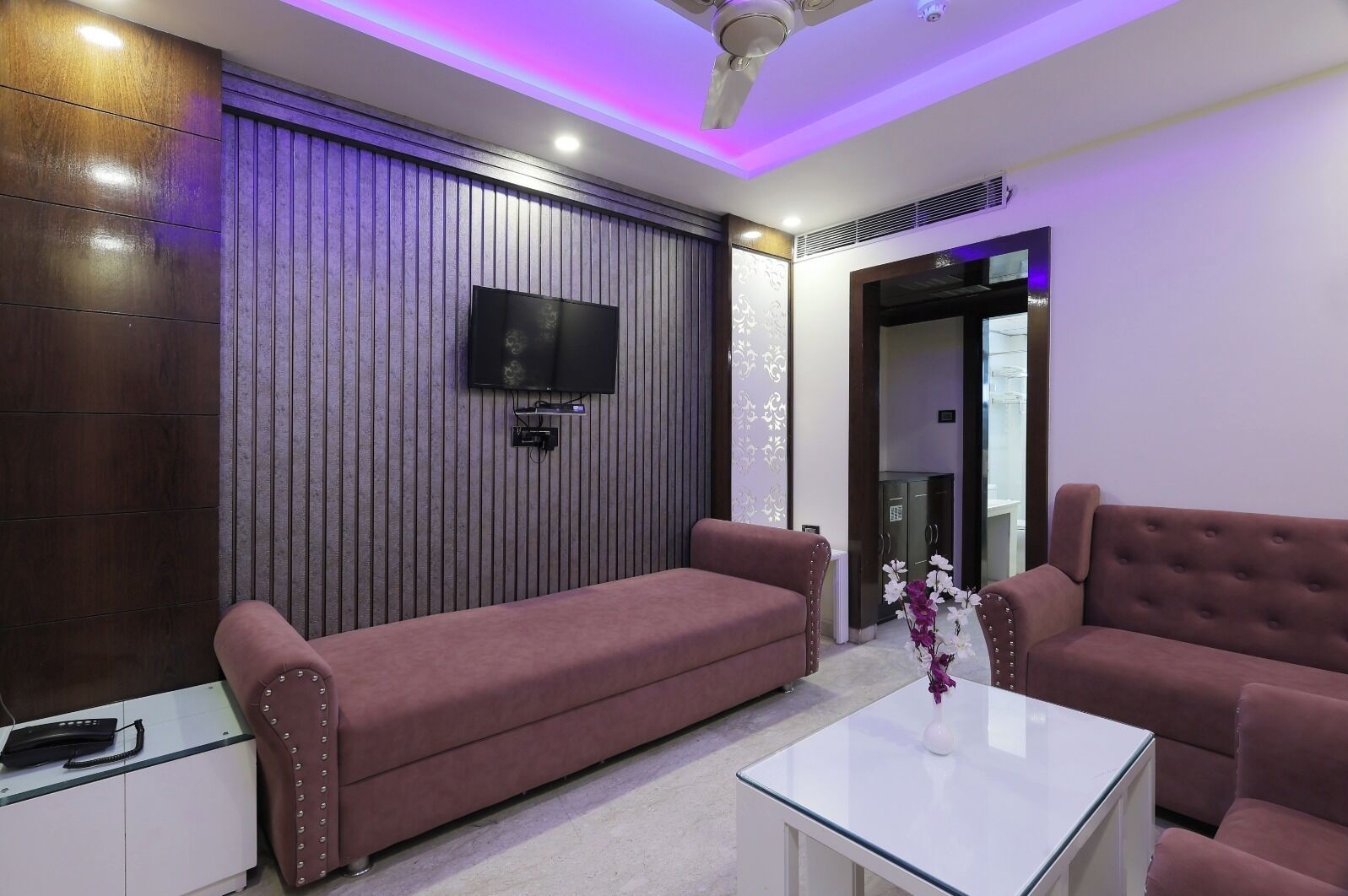 A modern living room with a sofa, a coffee table, and a flat-screen TV mounted on a wooden wall.
