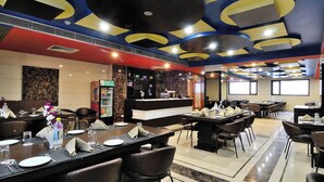 A restaurant with a modern ceiling design, a bar area, and a dining section with tables and chairs. - Crystal Ganga Heights 5 Min from Har Ki Pauri (Haridwar)