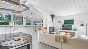 A modern kitchen with a built-in oven and a large stove, a cozy seating area with a sofa and a TV, and a large window overlooking greenery.