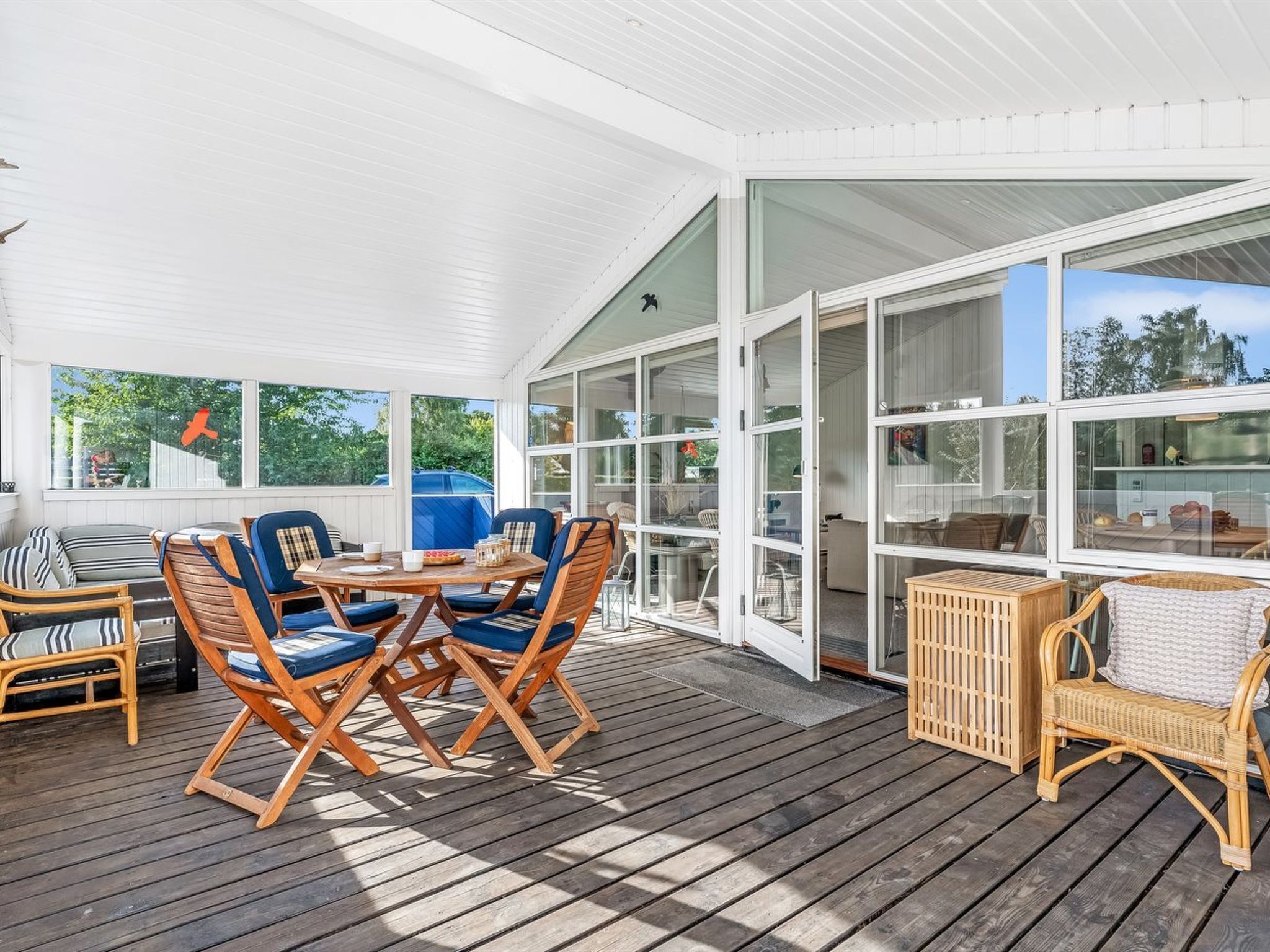A covered outdoor deck with wooden furniture, glass doors, and a view of the outdoors.