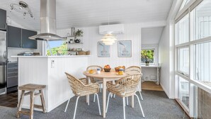 A modern kitchen with a central island, white cabinetry, and a dining area with wicker chairs.