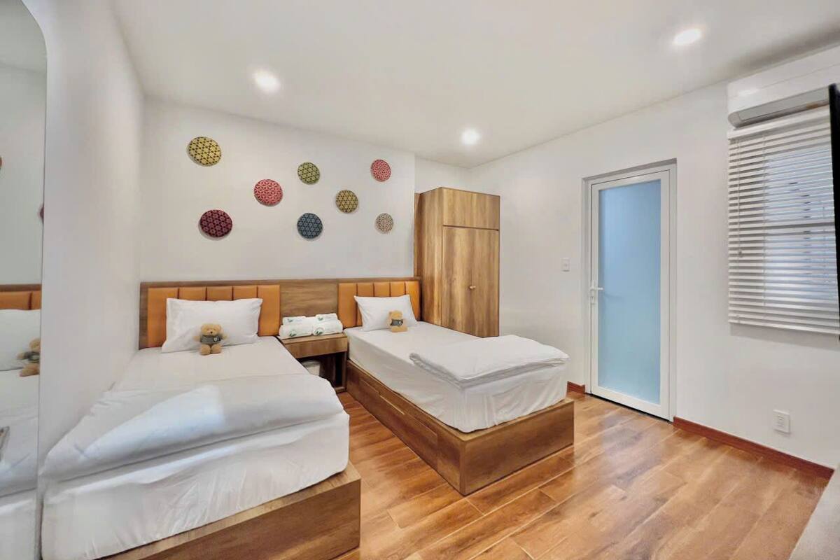 A modern bedroom with two beds, a wooden wardrobe, and decorative wall art.