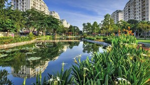 Ein friedlicher Stadtpark mit einem Teich, der sich spiegelt, üppigem Grün und modernen Wohngebäuden im Hintergrund.