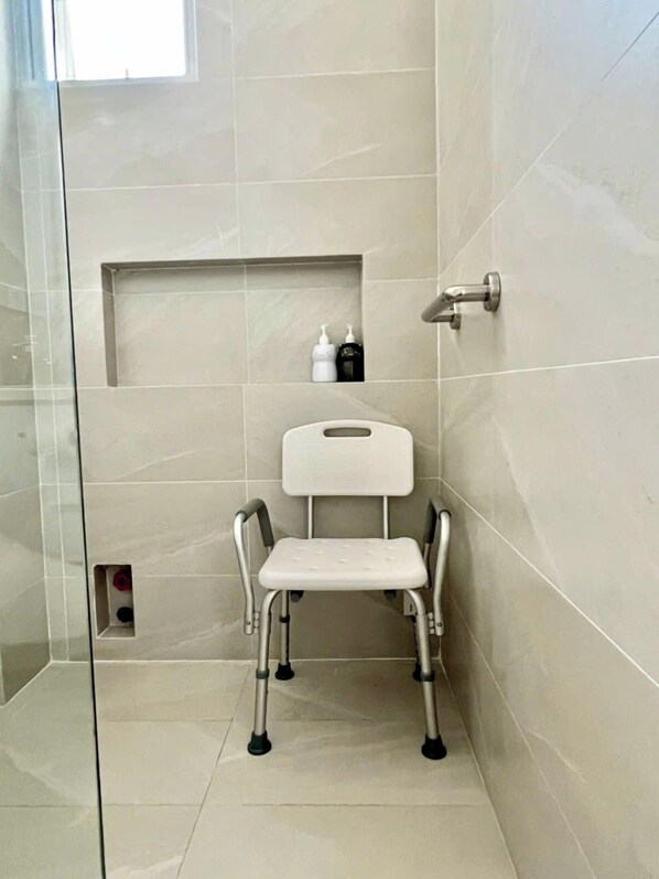 A bathroom with a shower stall, a white toilet with a backrest, and a shelf with toiletries. - C'est La Vie Homestay (Ho Chi Minh City)