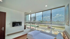 Ein Schlafzimmer mit einem Bett, einem an der Wand befestigten Fernseher, einem Fenster mit Blick auf die Stadt und einem Holzboden.