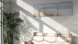 Ein Zimmer mit einem beige farbenen Sofa, einer großen Kübelpflanze und einer Wand mit drei gerahmten Kunstwerken.